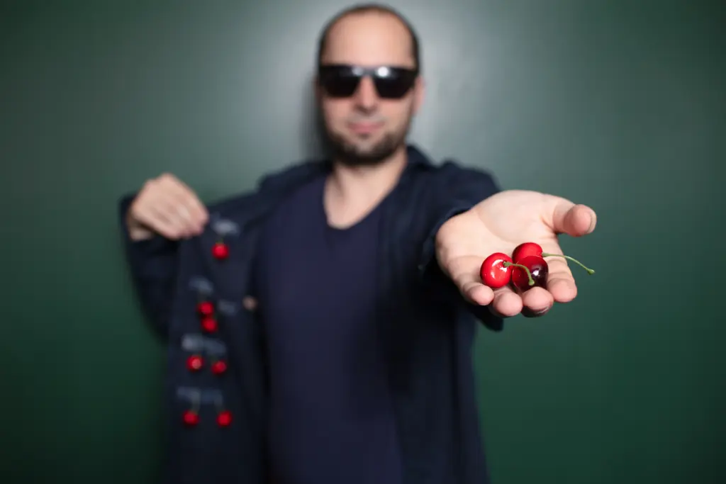 Malchus Kern mit Sonnenbrille streckt in der offenen Hand Kirschen in die Kamera.