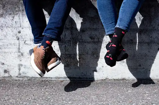 Bild zweier Beinpaare in Jeans und Socken mit Kirschmuster.