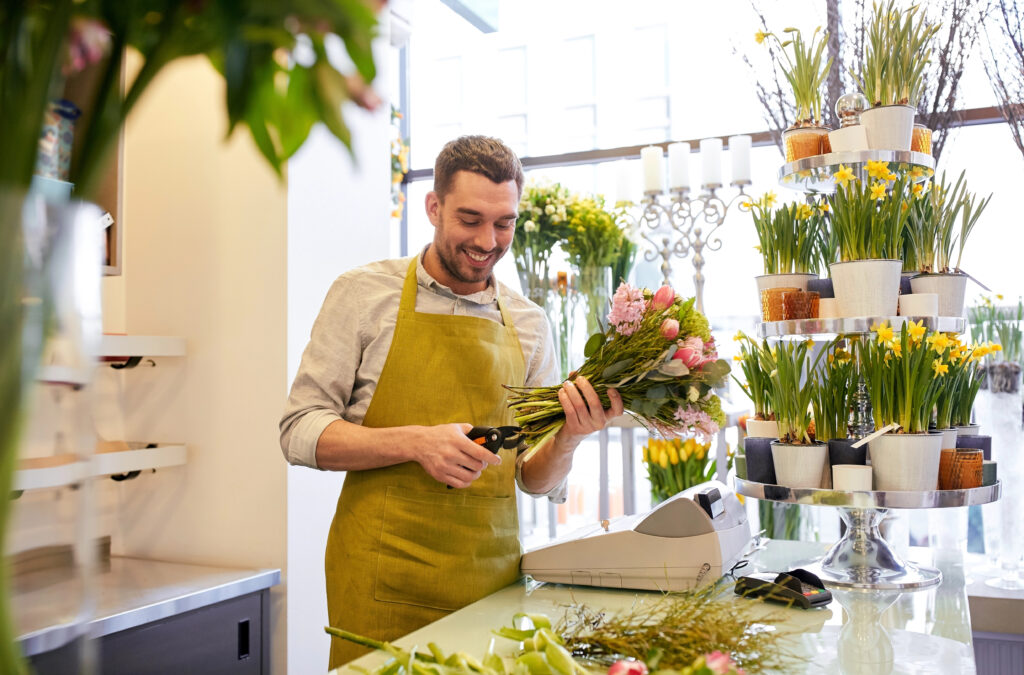 Bild von einem fröhlichen Florist beim Zuschneiden eines Blumenstraußes.