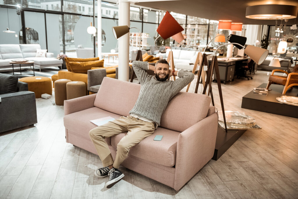 Bild eines jungen Mannes im Möbelladen, er sitzt zufrieden zurückgelehnt auf einem Sofa.