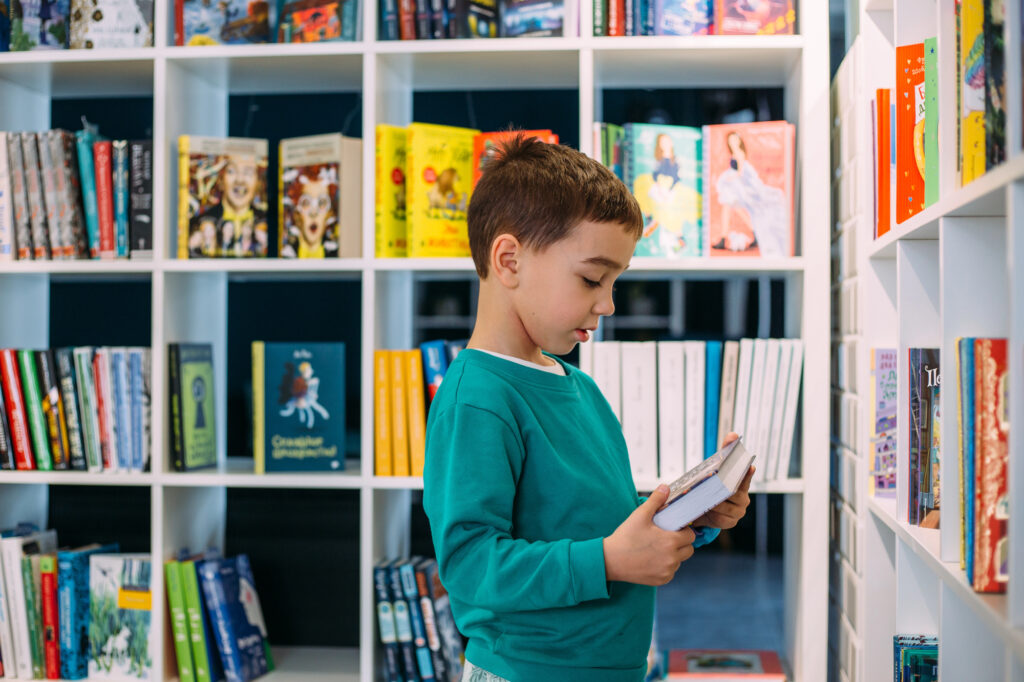 Bild eines Jungen in einem Buchladen, er betrachtet ein Buch in seinen Händen.