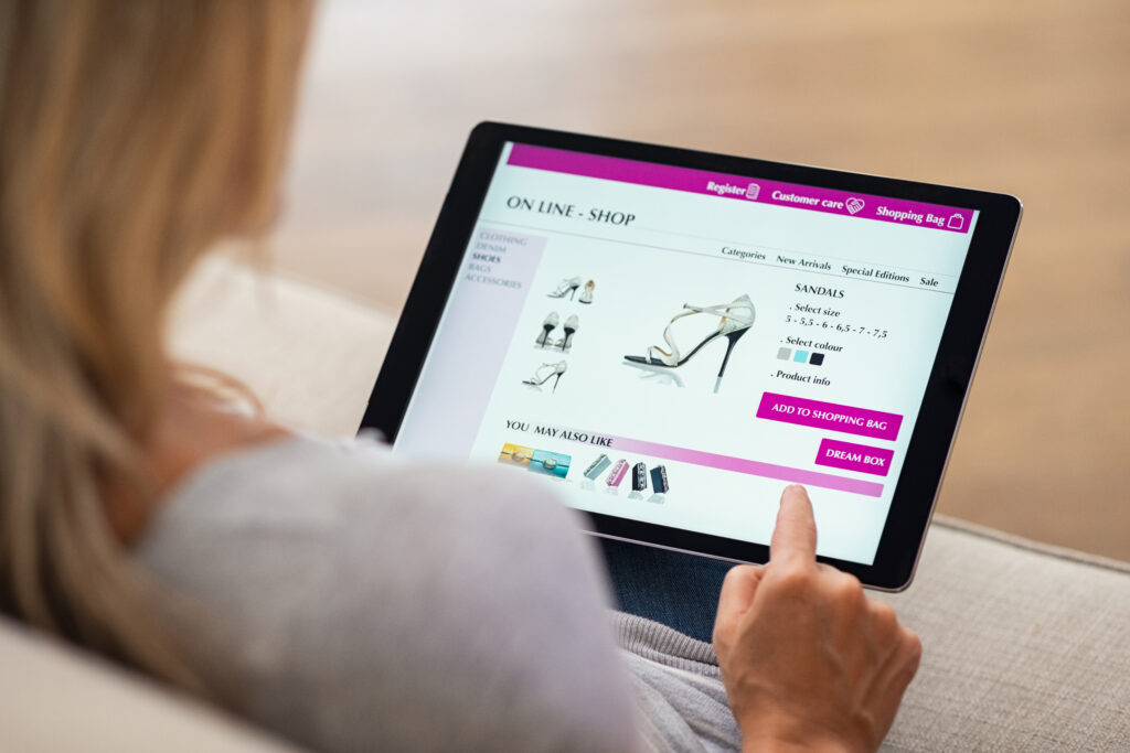 Bild über die Schulter einer Frau beim Online-Shoppen (nach Schuhen) auf einem Tablet.